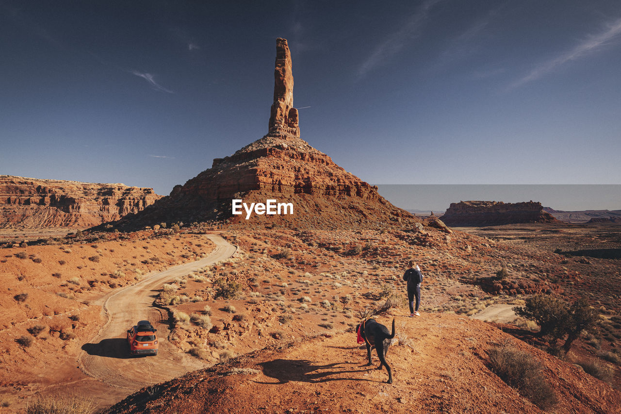 A woman with a child and a dog is standing on a hill at valley of gods