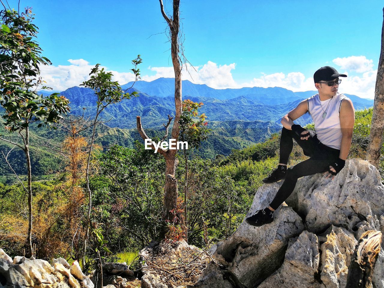 Man sitting on rock against sky