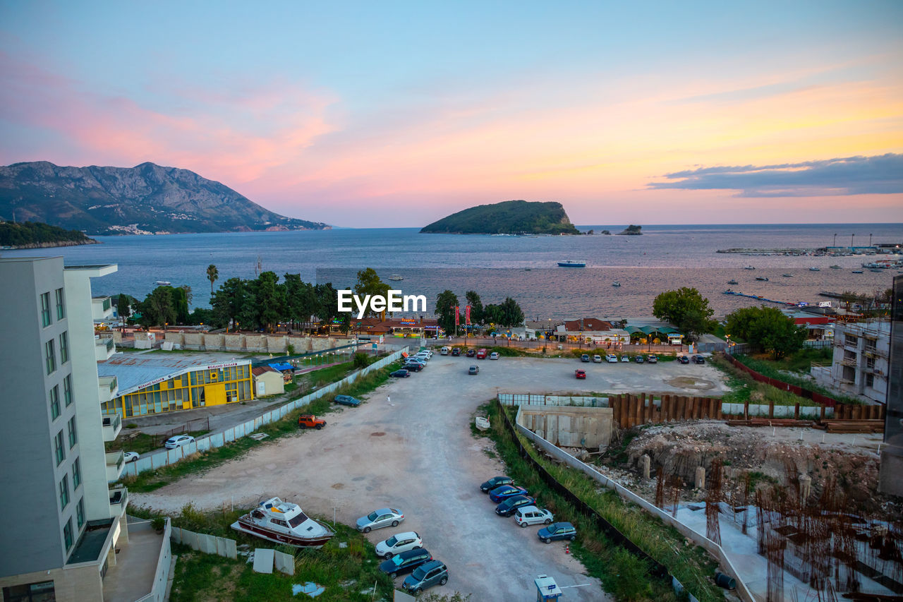 HIGH ANGLE VIEW OF CITY BY SEA AGAINST SKY AT SUNSET