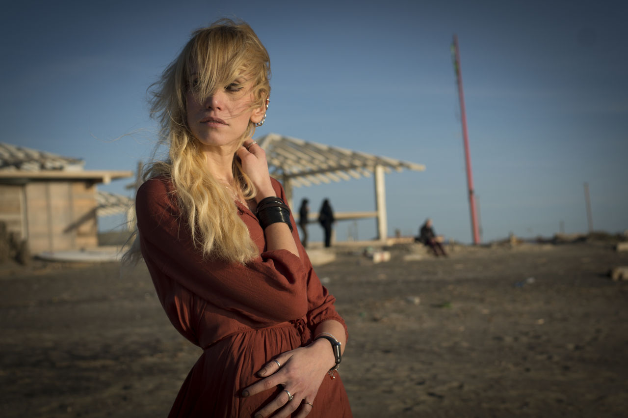 Thoughtful woman with tousled hair standing on field against sky