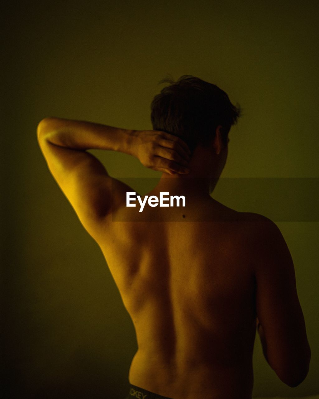 Rear view of shirtless man standing against gray background