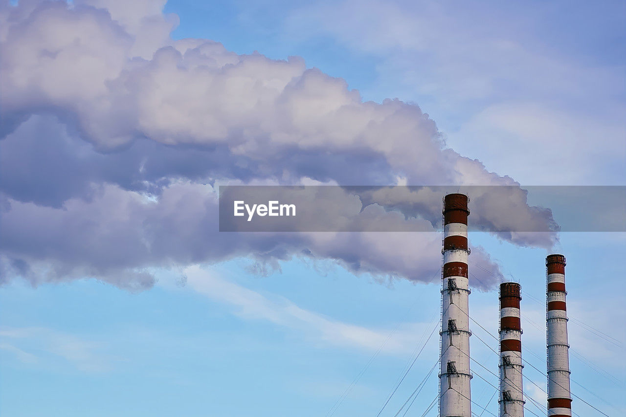 sky, cloud, smoke stack, factory, industry, power generation, tower, nature, smoke, technology, pollution, environmental issues, environment, built structure, air pollution, no people, architecture, blue, day, power station, outdoors, building exterior, outdoor structure, low angle view, electricity, fossil fuel, communication, wind, poisonous, pipe - tube, business finance and industry, power supply, oil industry