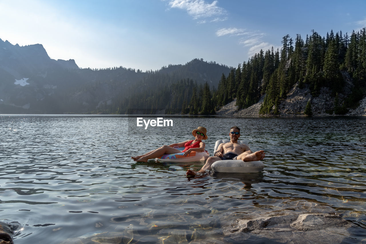 Couple on inflatable rings in lake against sky