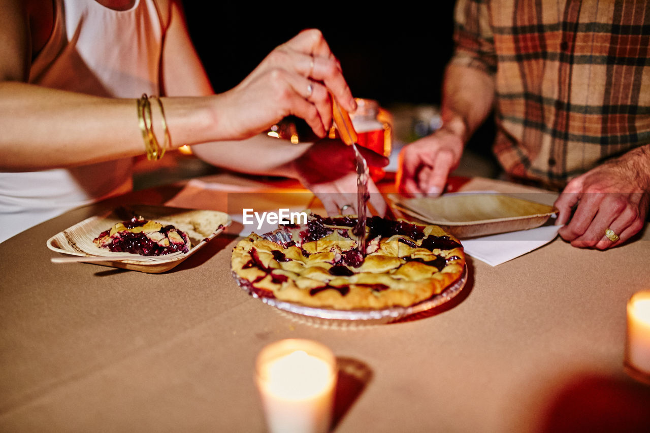 Midsection of couple eating tarts on table