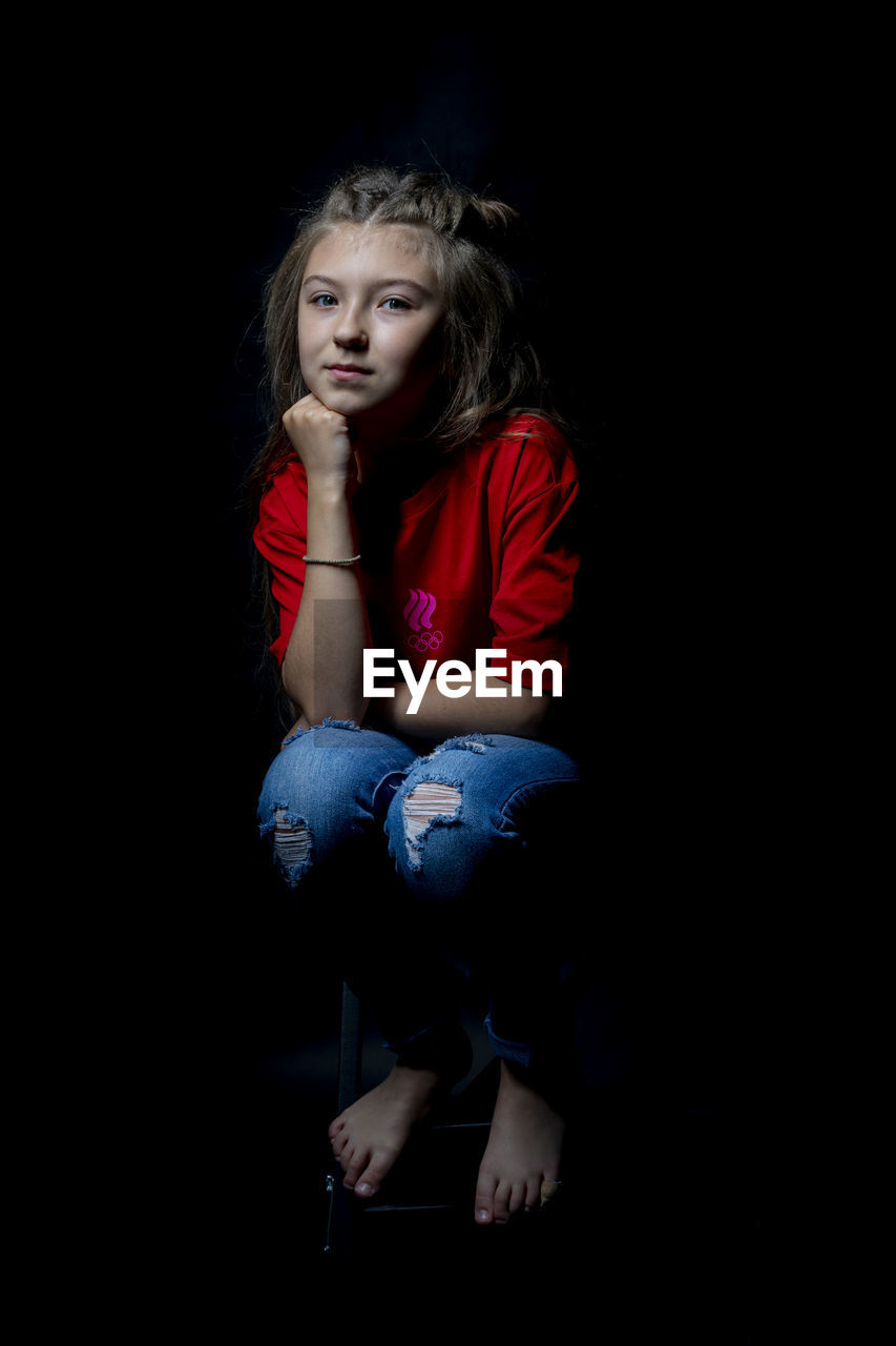 Portrait of girl sitting against black background