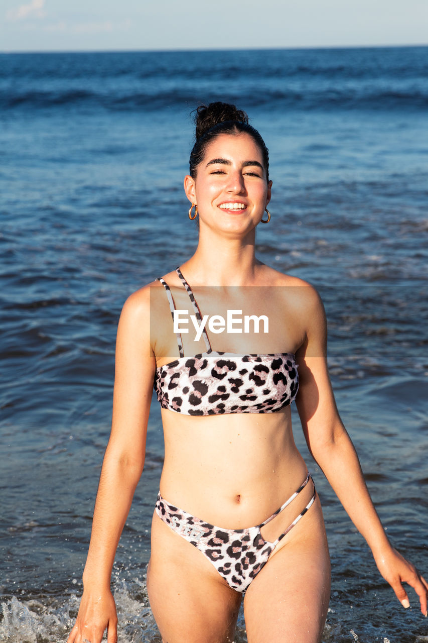 Portrait of woman in bikini standing at beach