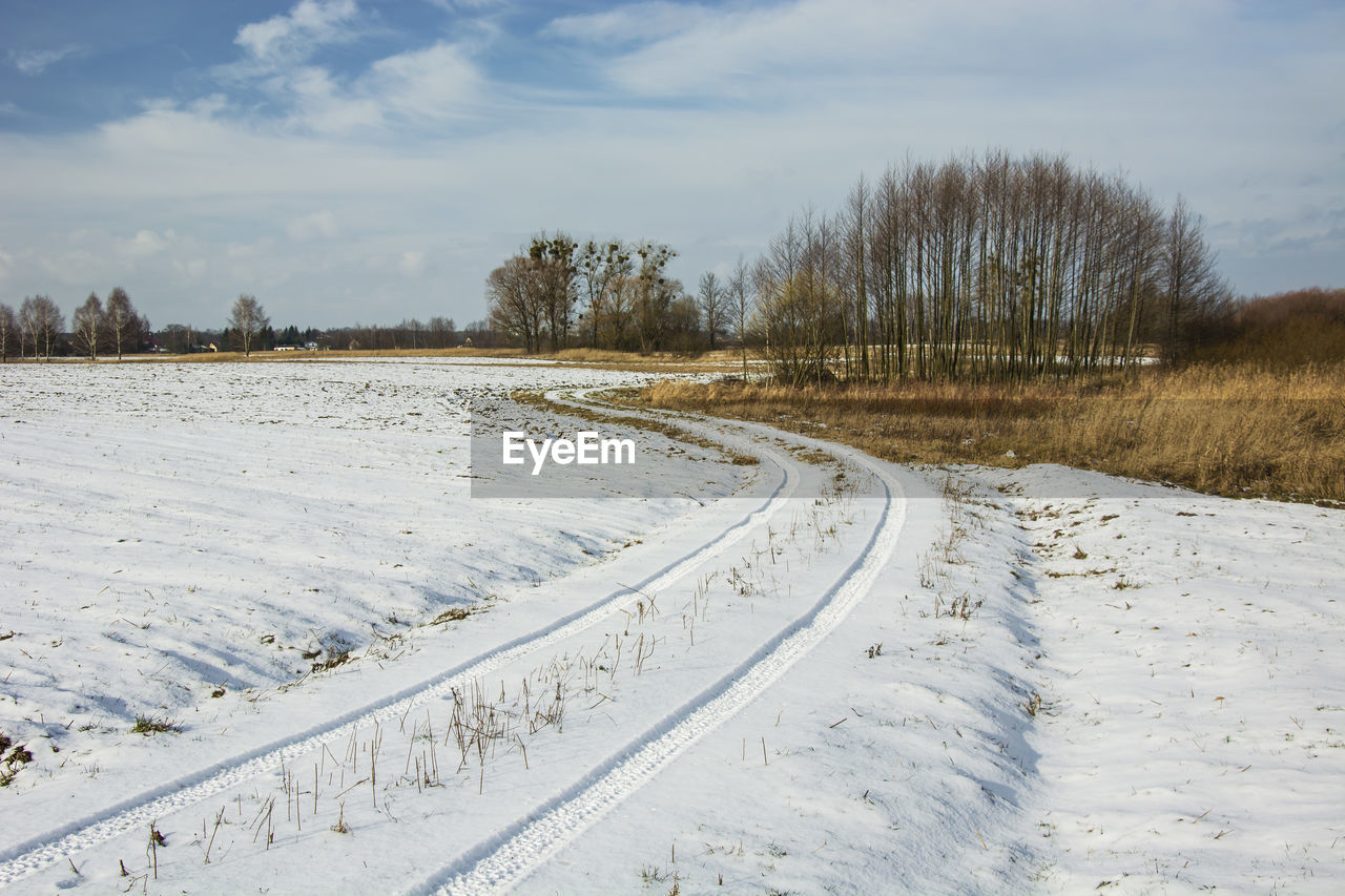 Traces of wheels in the snow on a dirt road, trees and sky, winter view