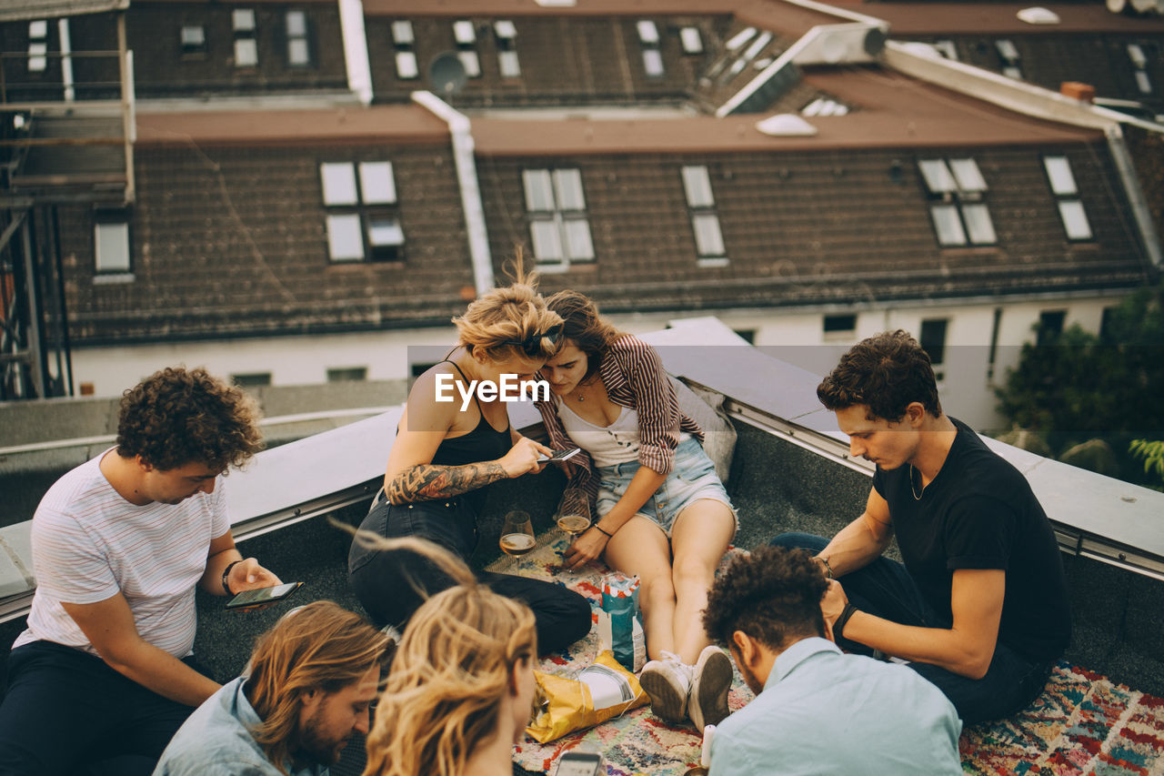 Male and female friends using smart phones while sitting on terrace during party