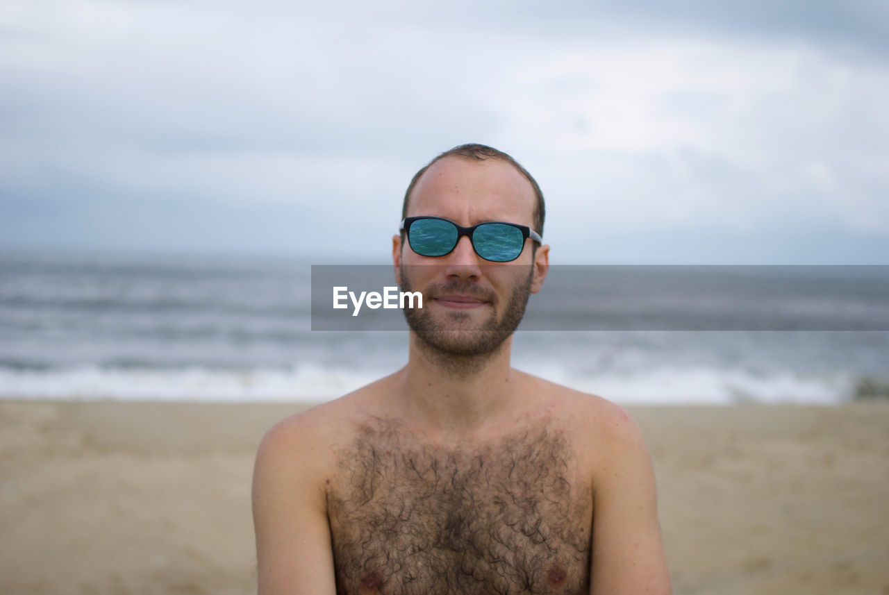 Man wearing sunglasses white standing at beach against sky
