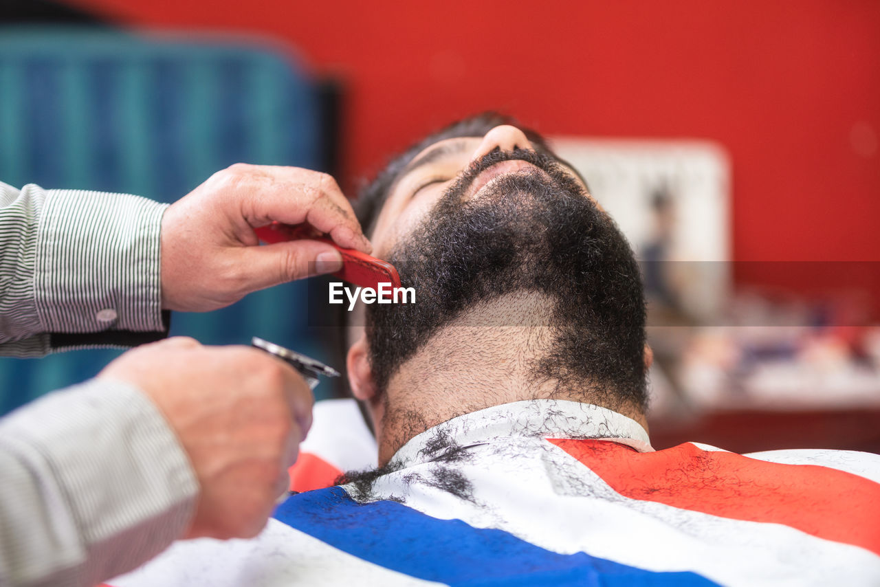 Cropped hands of barber shaving male customer beard in salon