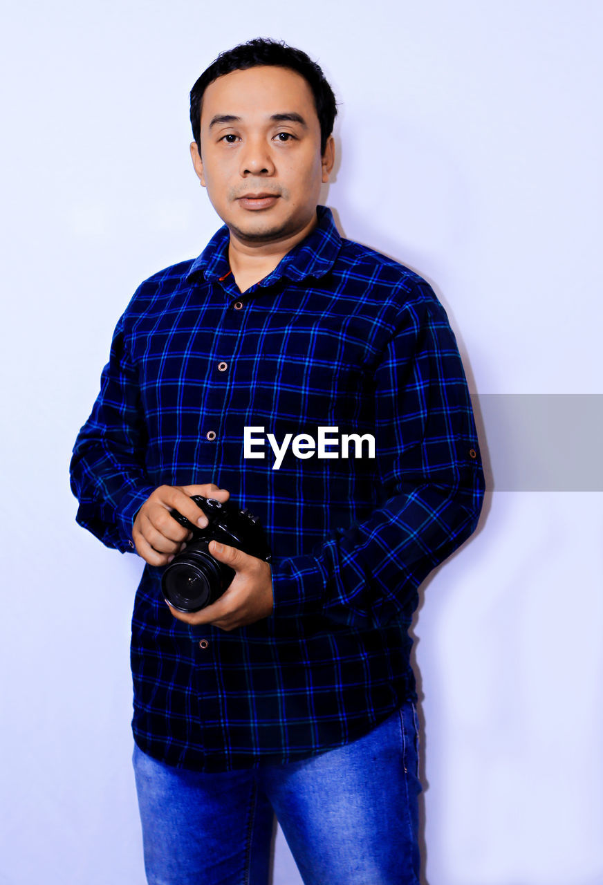 Portrait of man holding camera against white background