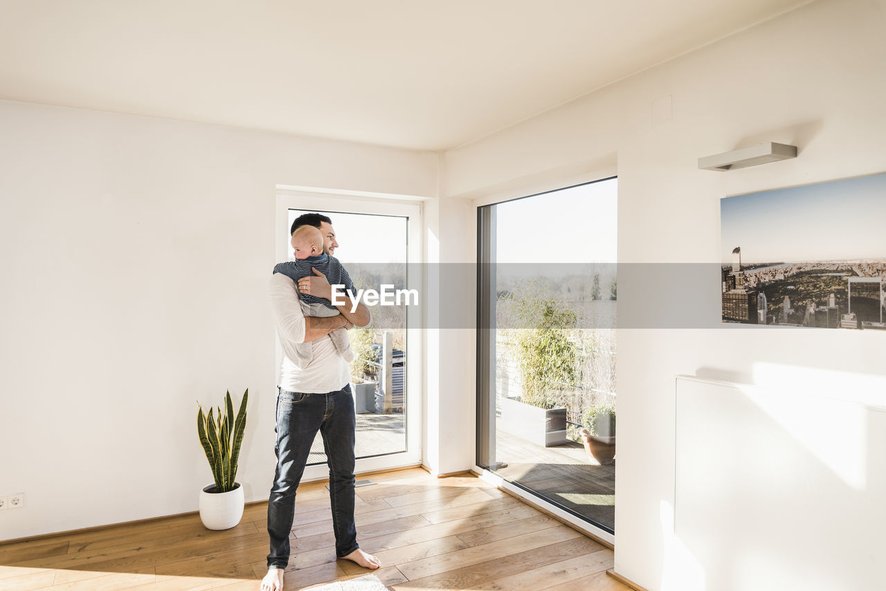 Father holding and hugging his baby son, standing in comfortable home