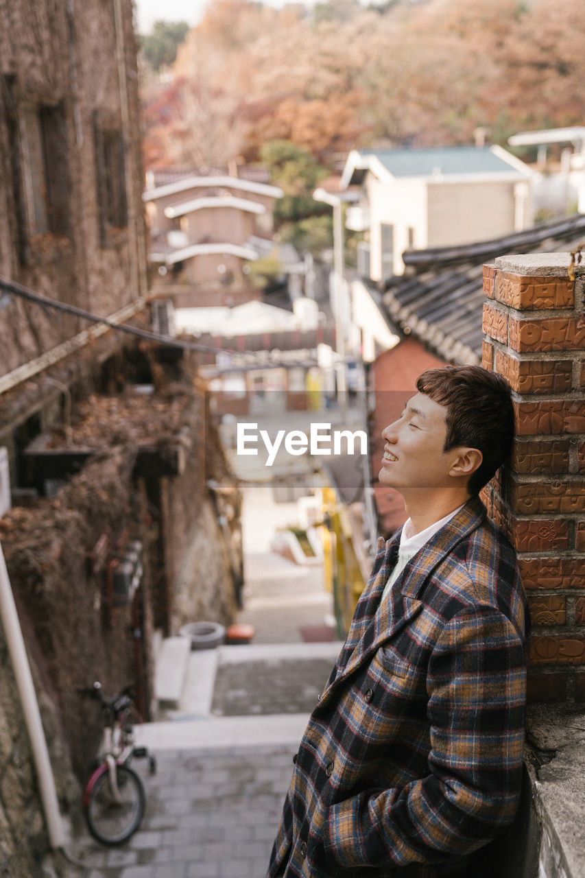 SIDE VIEW OF MAN STANDING AGAINST BUILDING IN CITY