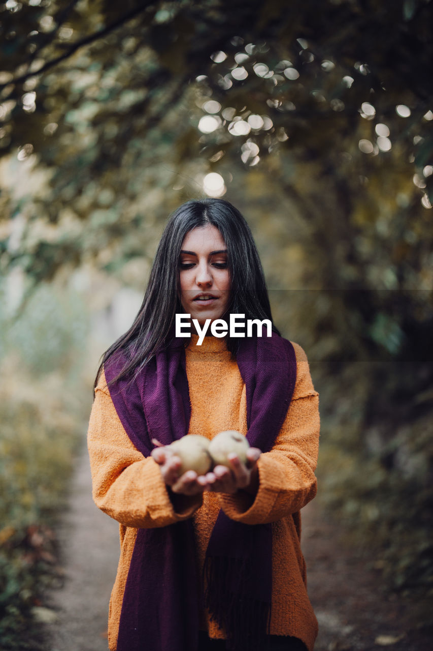 Woman wearing scarf holding fruits in forest