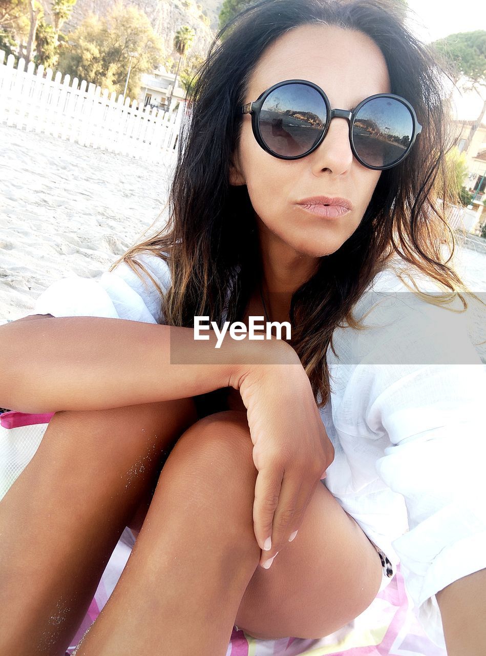 sunglasses, women, fashion, adult, young adult, one person, glasses, summer, long hair, bikini, trip, vacation, hairstyle, leisure activity, sitting, relaxation, holiday, beach, swimwear, sunlight, portrait, black hair, clothing, nature, lifestyles, day, water, land, brown hair, sun, three quarter length, human leg, limb, outdoors, travel, sunbathing, human hair, looking at camera, female, blond hair, smiling, enjoyment, front view, happiness, casual clothing, sea, carefree, photo shoot, sunny, travel destinations, emotion