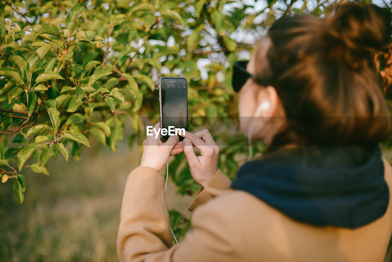 REAR VIEW OF WOMAN PHOTOGRAPHING THROUGH SMART PHONE