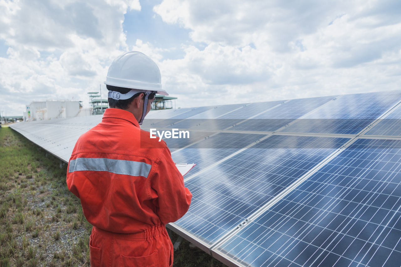 Engineer standing amidst solar panel against cloudy sky