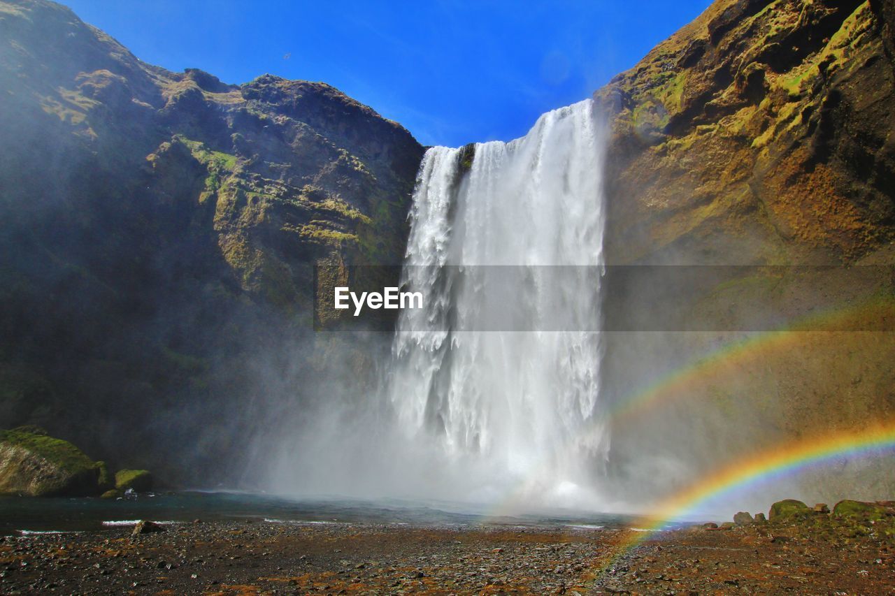 Scenic view of waterfall and rainbow against sky