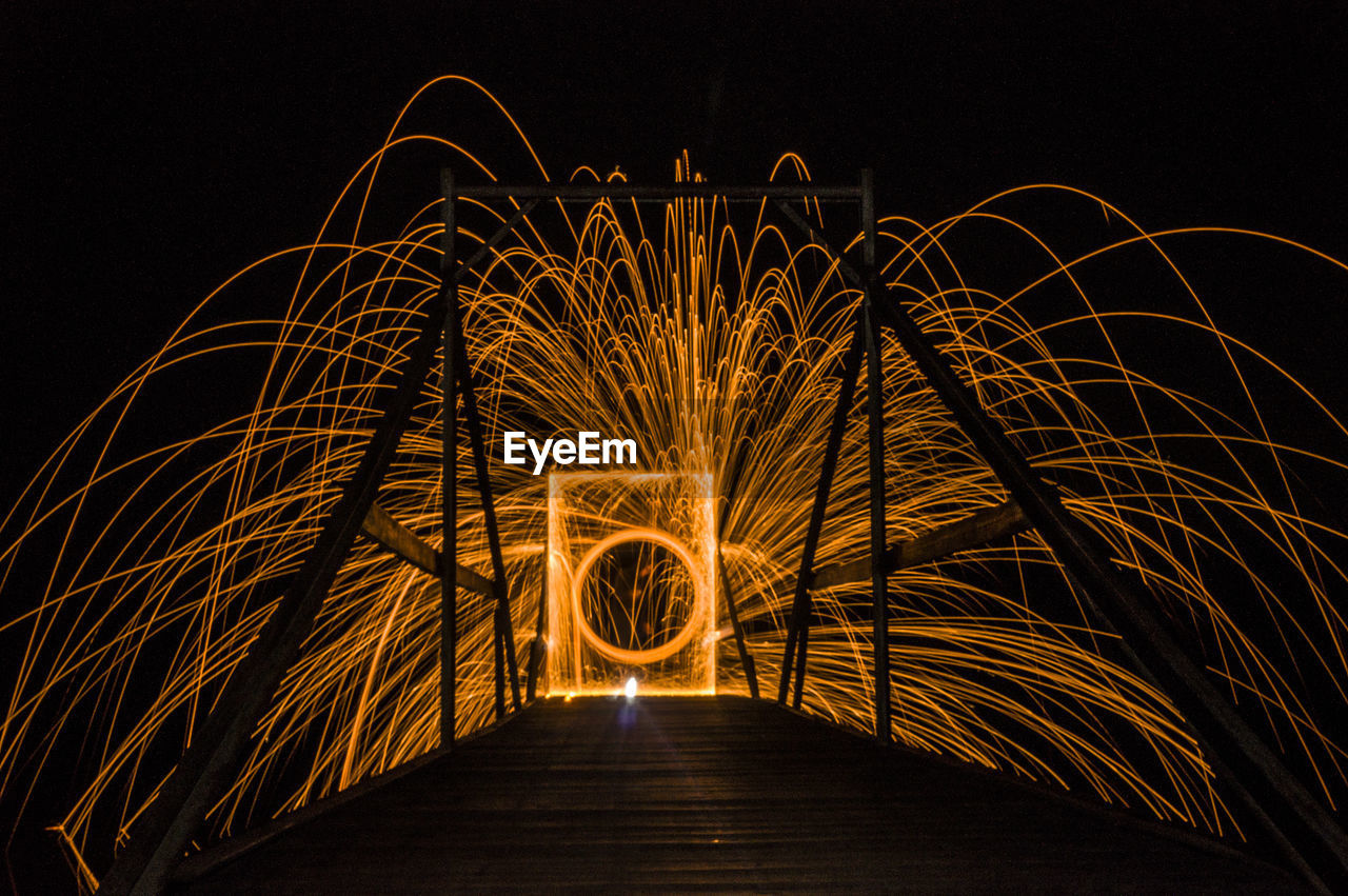 Illuminated wire wool spinning on bridge at night