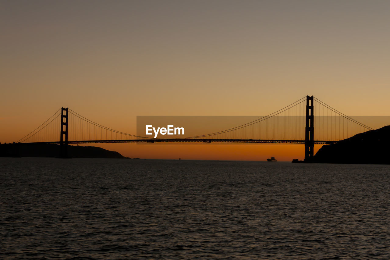 Silhouette golden gate bridge over sea against clear sky during sunset