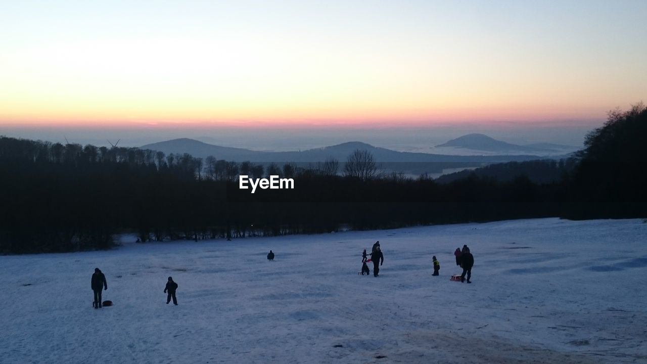 SILHOUETTE PEOPLE ON SNOW LANDSCAPE AGAINST SKY DURING SUNSET