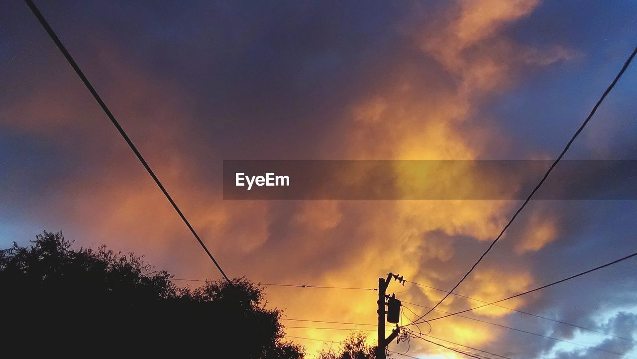 Low angle view of electricity pylon against cloudy sky