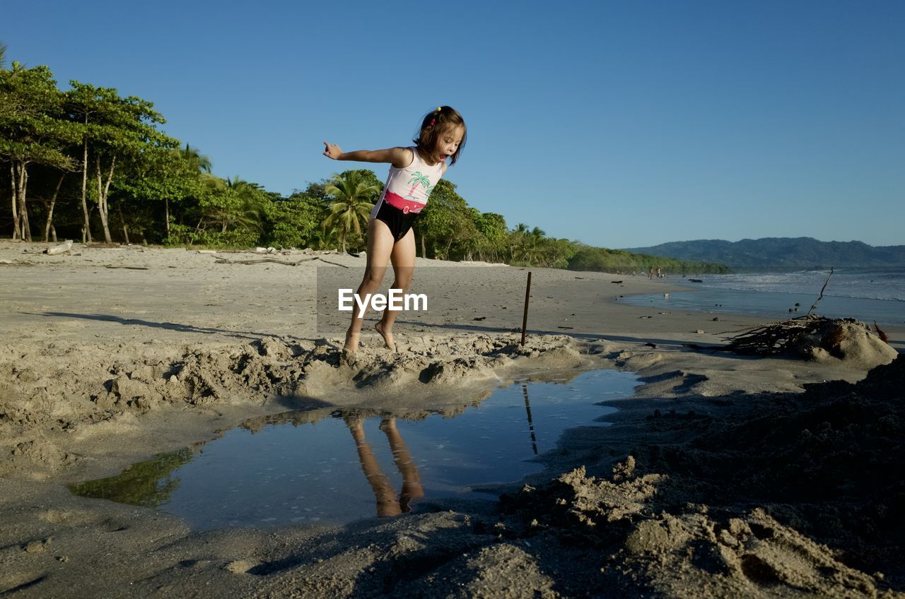 Full length of girl jumping at beach against clear sky