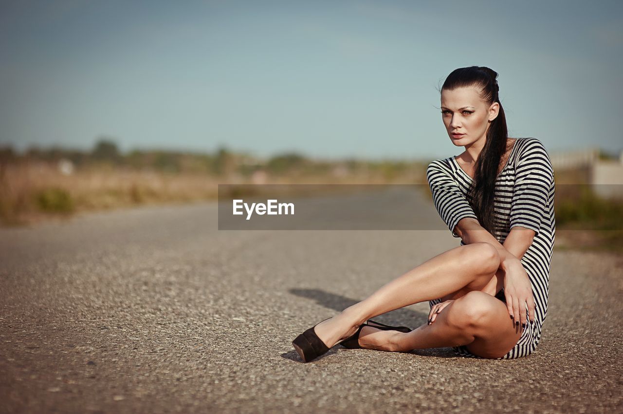 Portrait of young woman sitting on road against clear sky