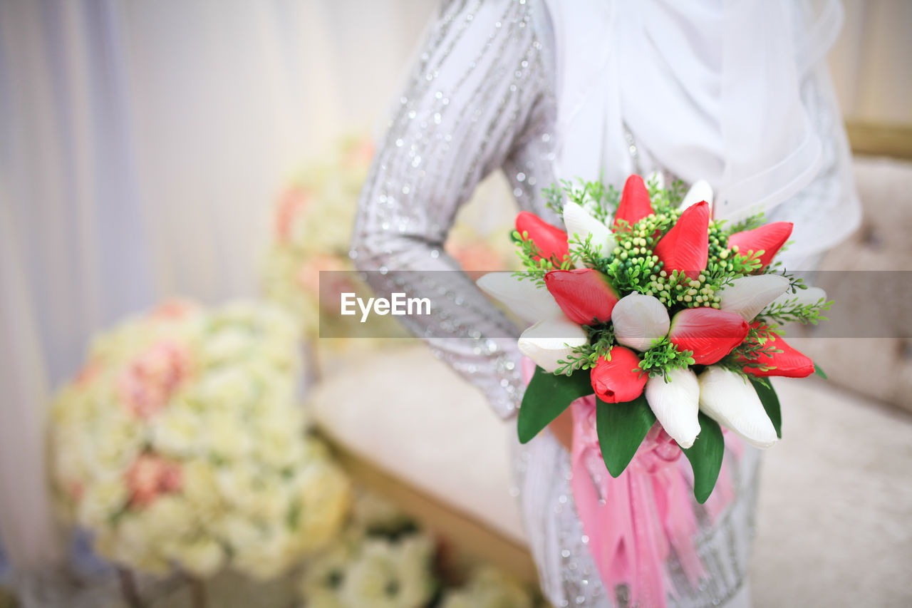 flower, flowering plant, plant, wedding dress, bouquet, one person, adult, flower arrangement, bride, women, floristry, celebration, midsection, event, pink, nature, wedding, newlywed, holding, dress, ceremony, beauty in nature, clothing, floral design, indoors, standing, decoration, freshness, lifestyles, life events, female, front view, focus on foreground, young adult, emotion, rose, petal, gift, gown, white, bunch of flowers, arrangement, spring, wedding ceremony, fashion, flower head, positive emotion, close-up