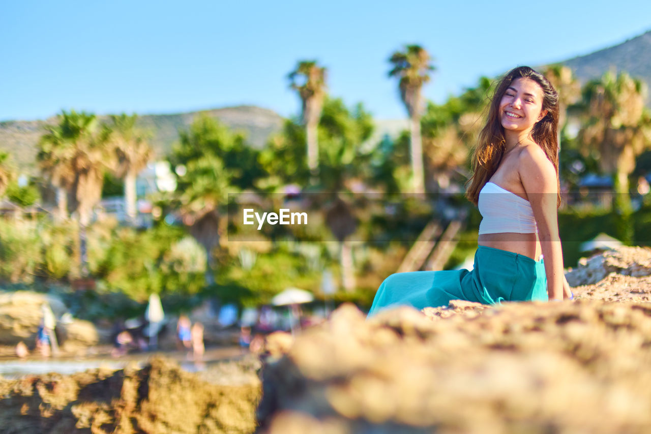 Smiling beautiful woman sitting on rock at beach