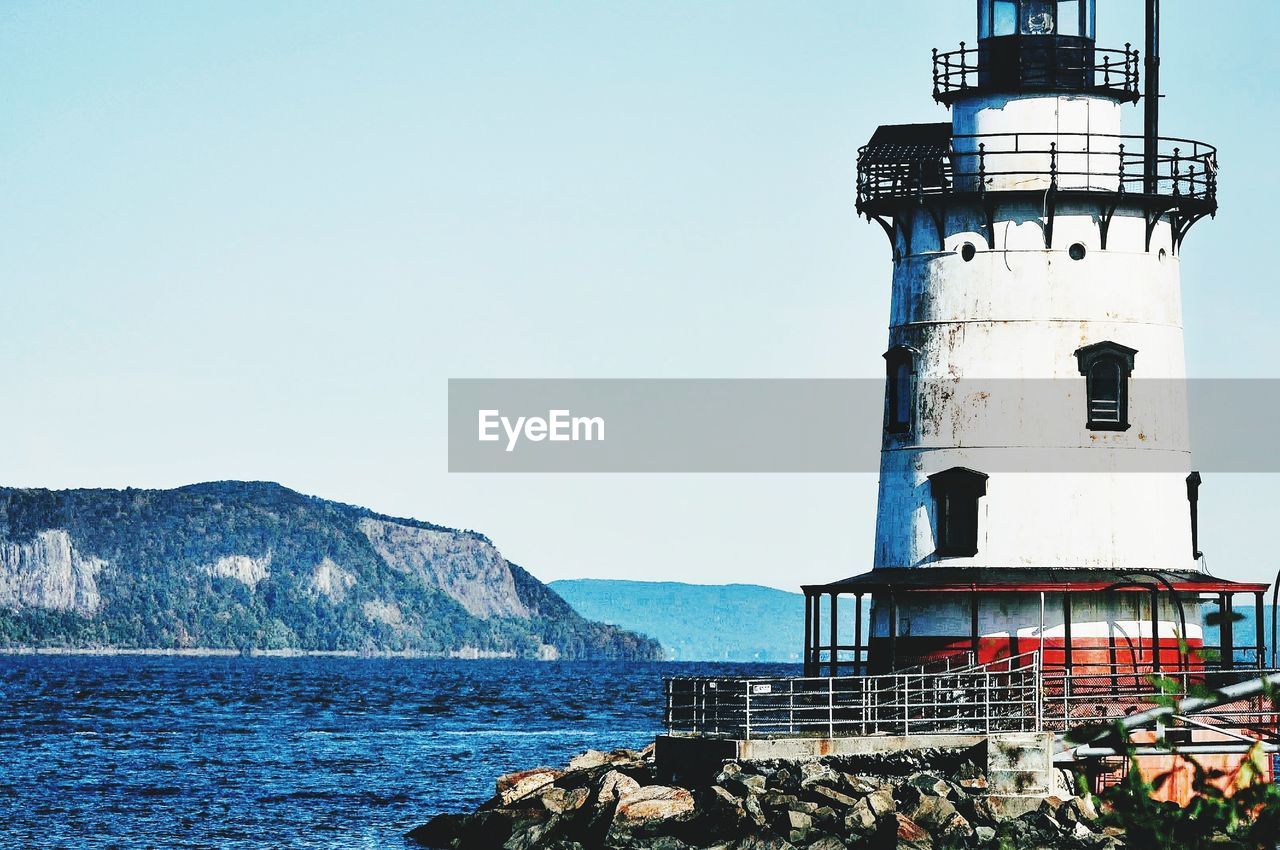 LIGHTHOUSE BY SEA AGAINST BUILDINGS