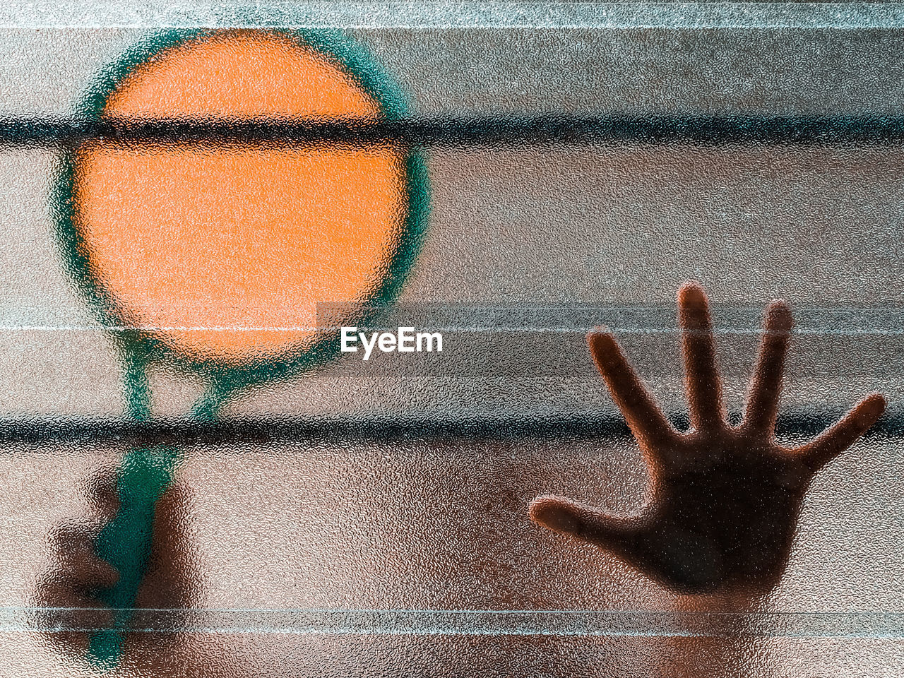 Close-up of a boy's hand holding a badminton racquet behing a textured glass window