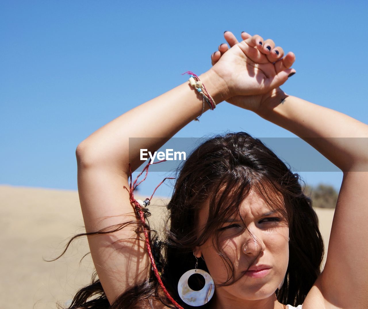 Thoughtful young woman with arms raised standing at beach against clear sky