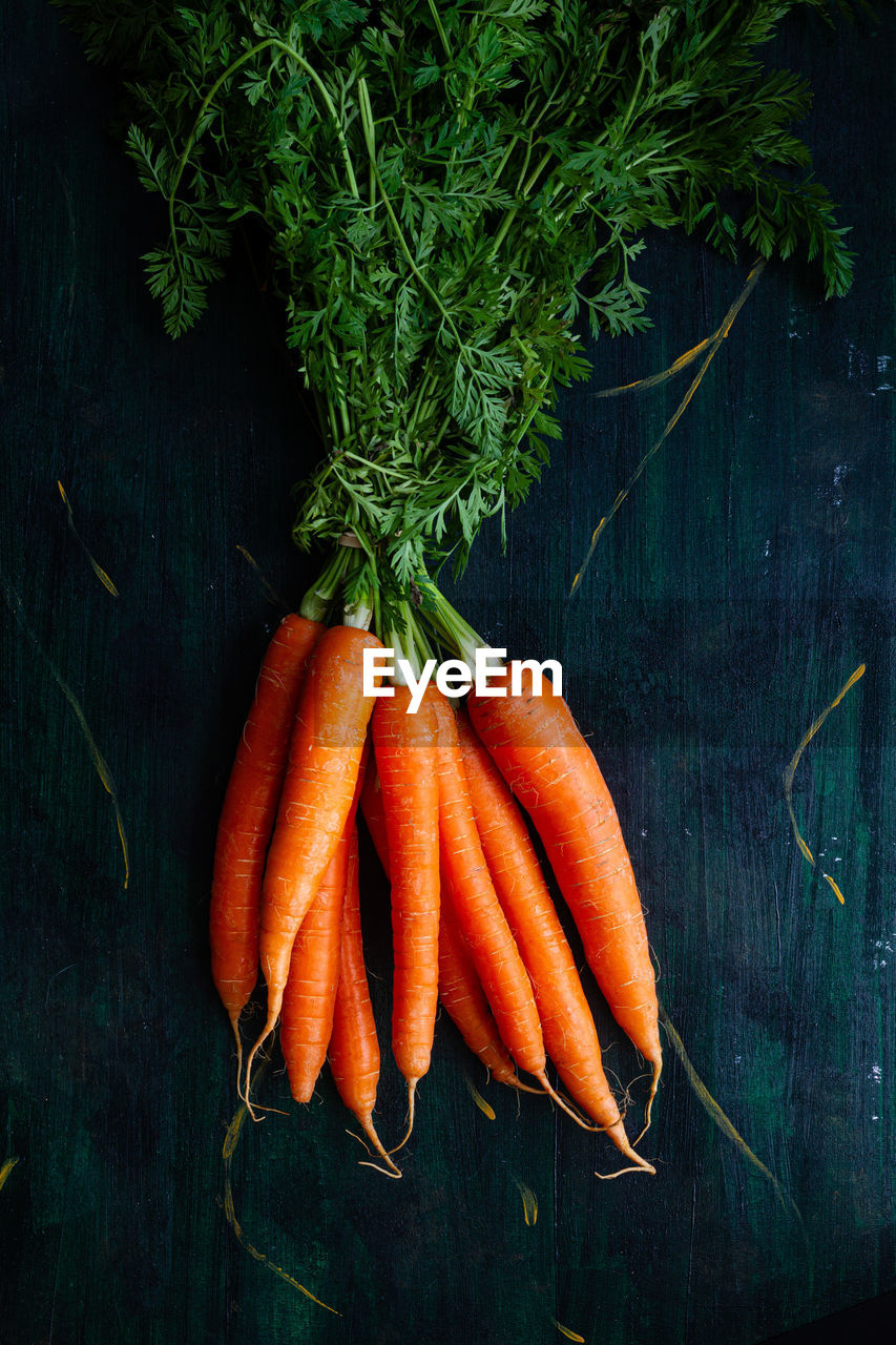 Top view of bunch of whole raw carrots with stems and leaves on wooden surface