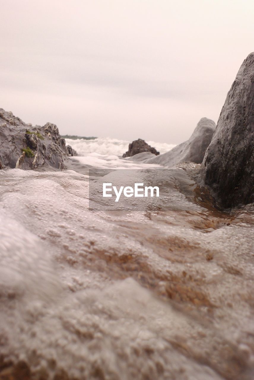 Surface level view of wet sand on beach by rocks against sky