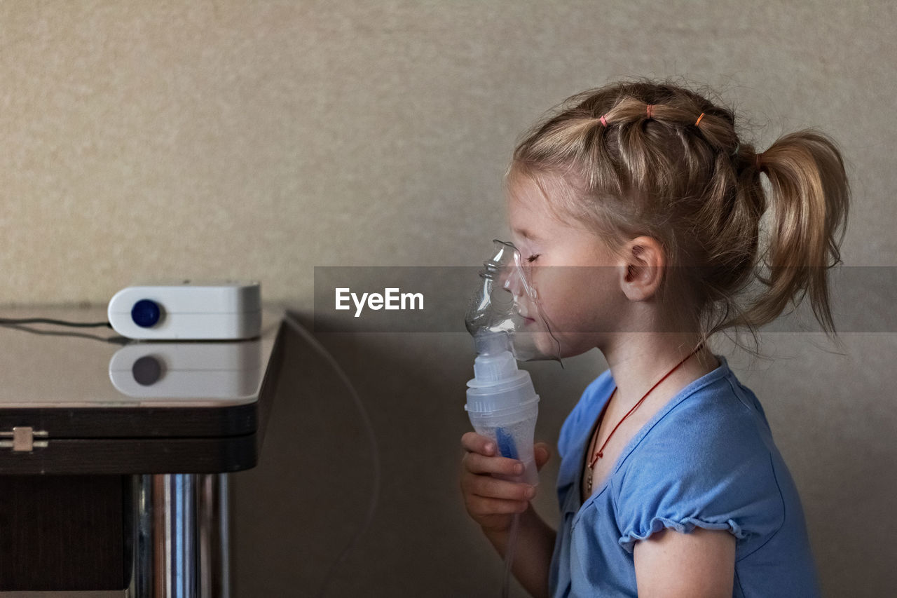 Side view of girl breathing with nebulizer at home