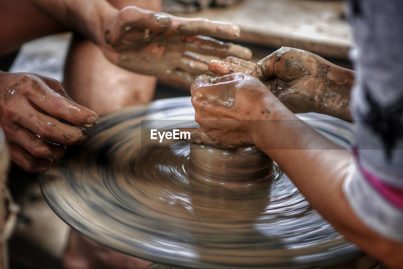 Cropped hands of potters making earthenware on pottery wheel