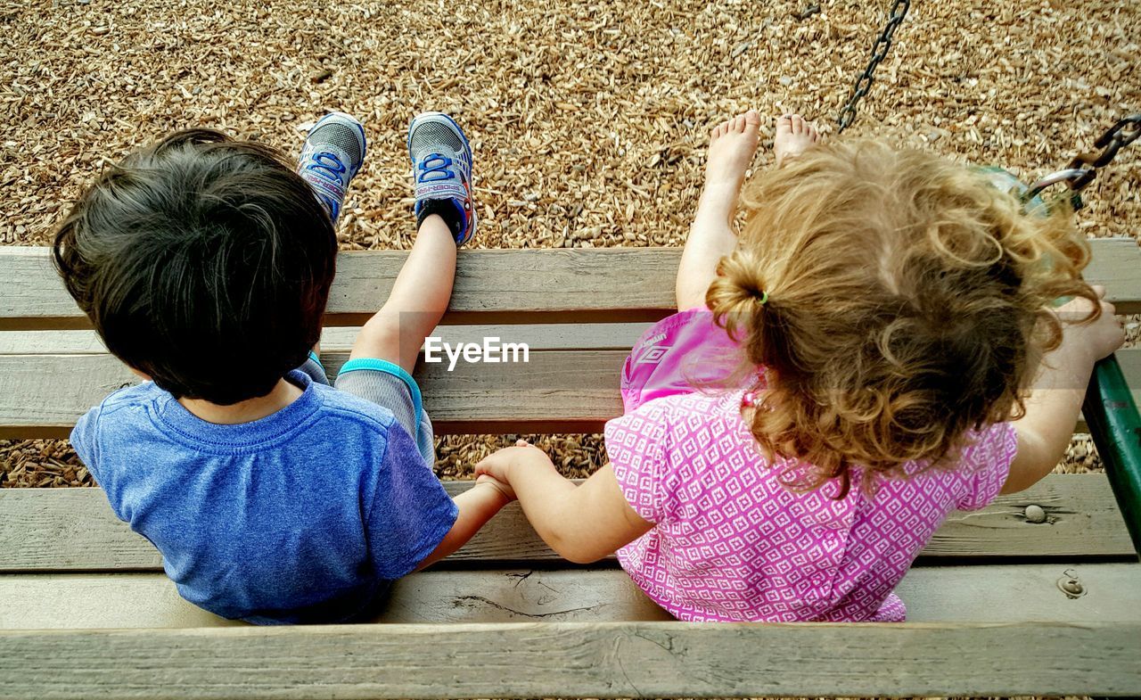 High angle view of siblings holding hands while sitting on bench