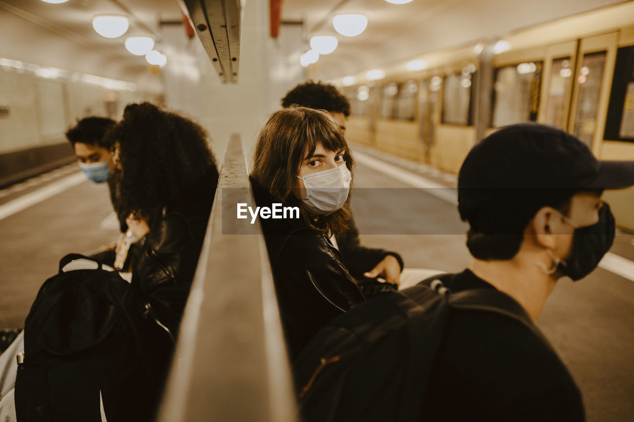 Young woman with friends sitting at subway station during pandemic