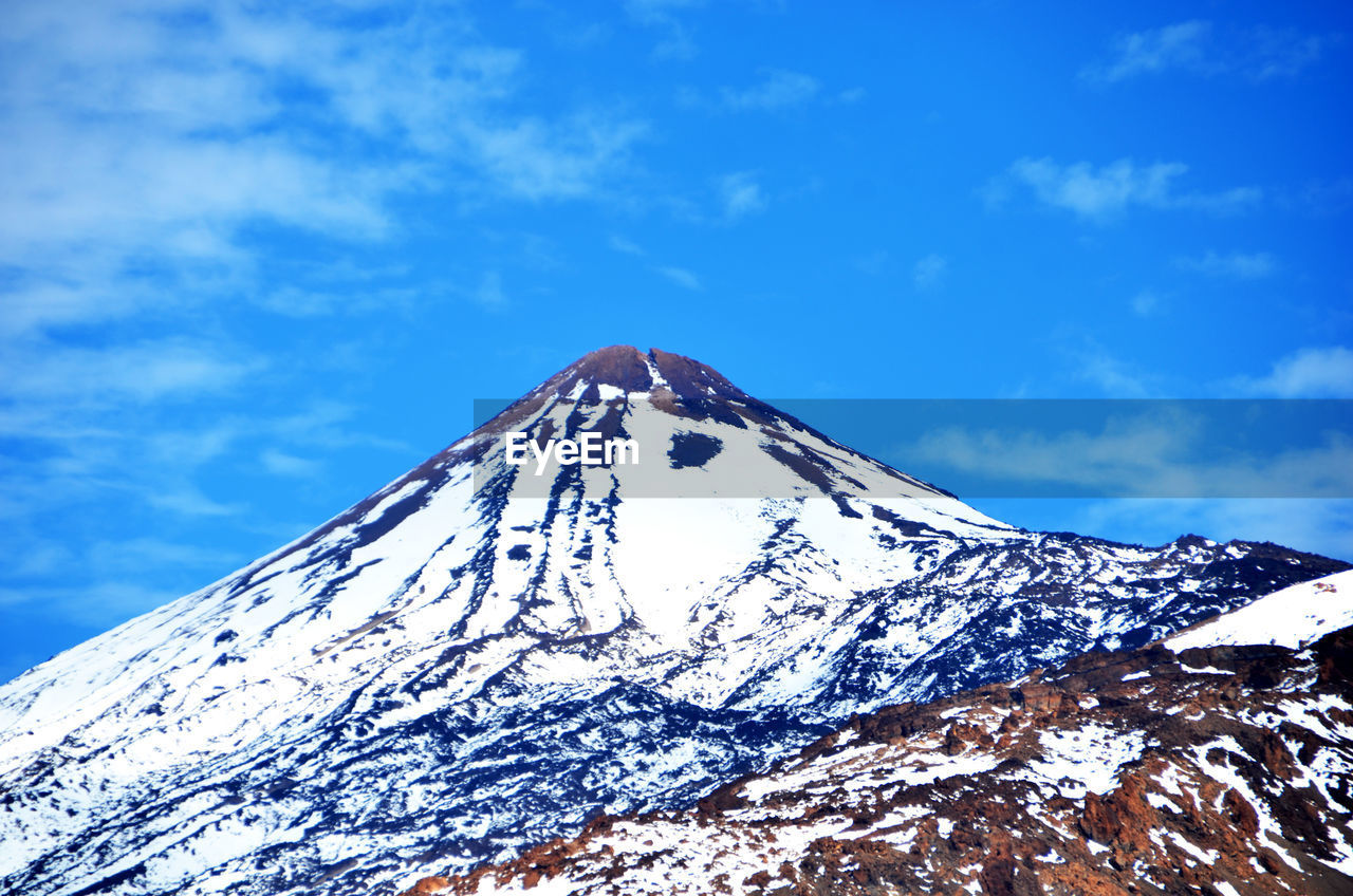 Low angle view of snow covered mountain against blue sky