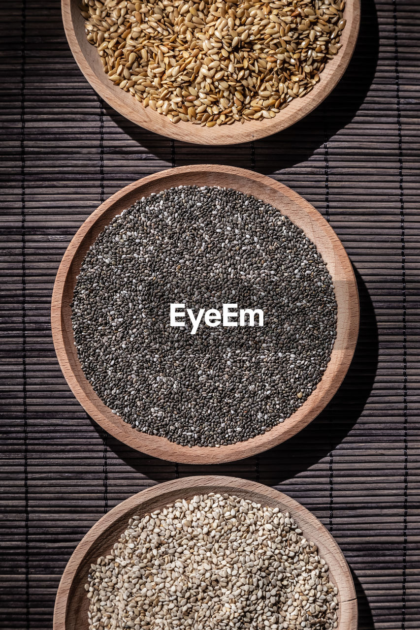 Sesame, chia and flax seeds in wooden dishes on wooden base. vertical format.