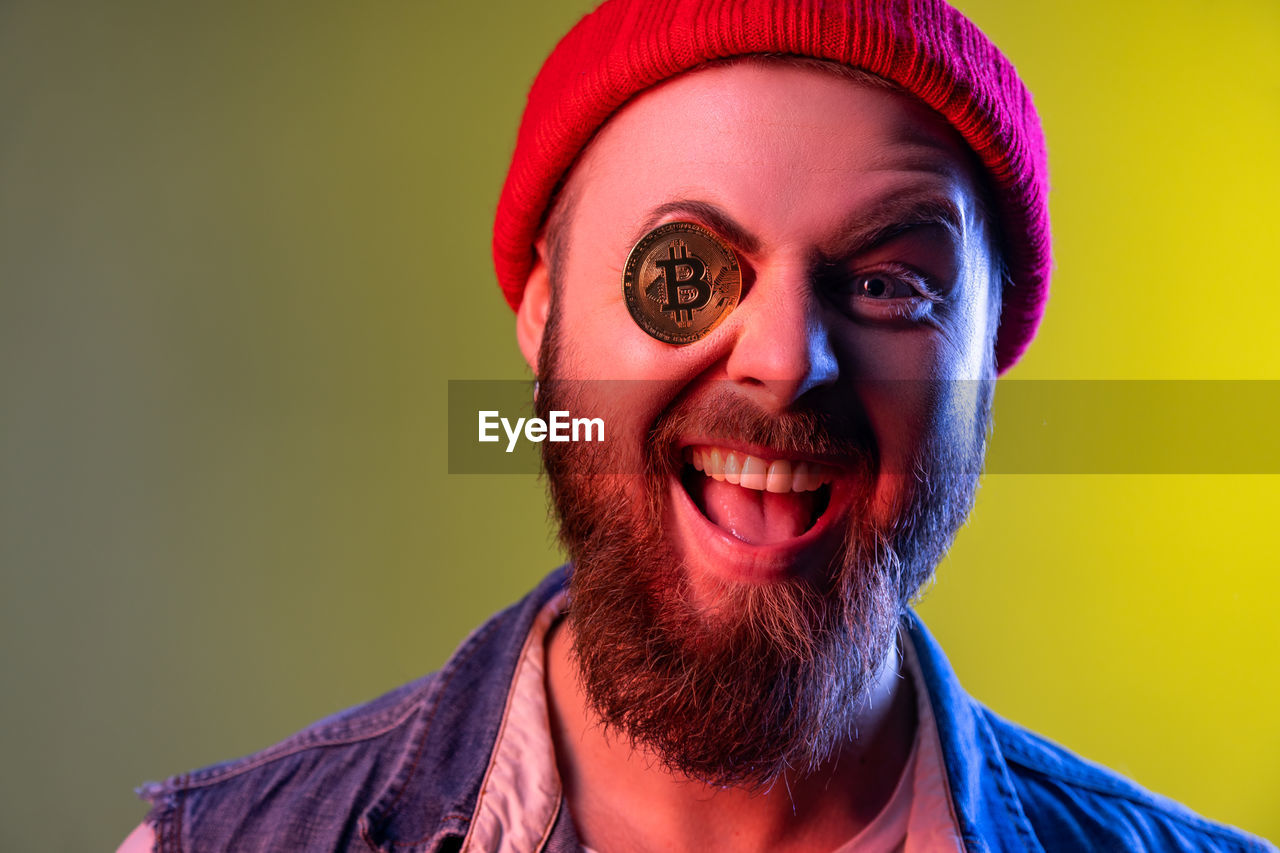 portrait, one person, headshot, facial hair, studio shot, adult, beard, colored background, emotion, human hair, looking at camera, smiling, human face, men, happiness, indoors, young adult, fun, red, human head, clothing, close-up, facial expression, person, front view, yellow, individuality, humor, hat, copy space, multi colored, cheerful, human mouth, celebration, mouth open, teeth