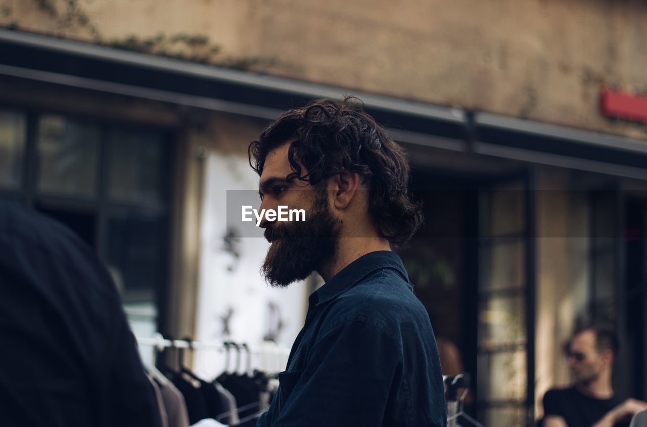 Side view of bearded young man looking away against building