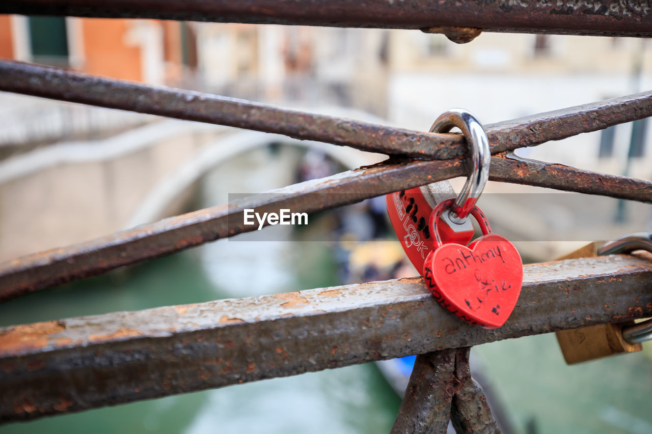 Close-up of love locks hanging on rusty metallic railing against canal in city