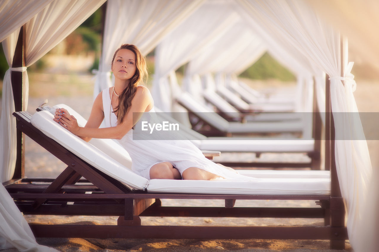 Portrait of beautiful young woman sitting on lounge chair at bench