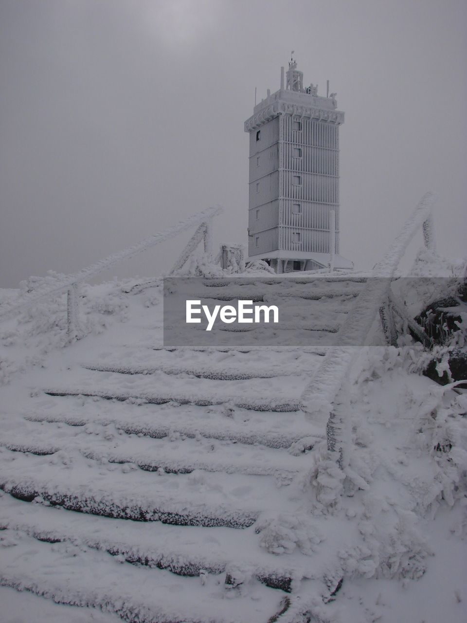 Snow covered land by building against sky