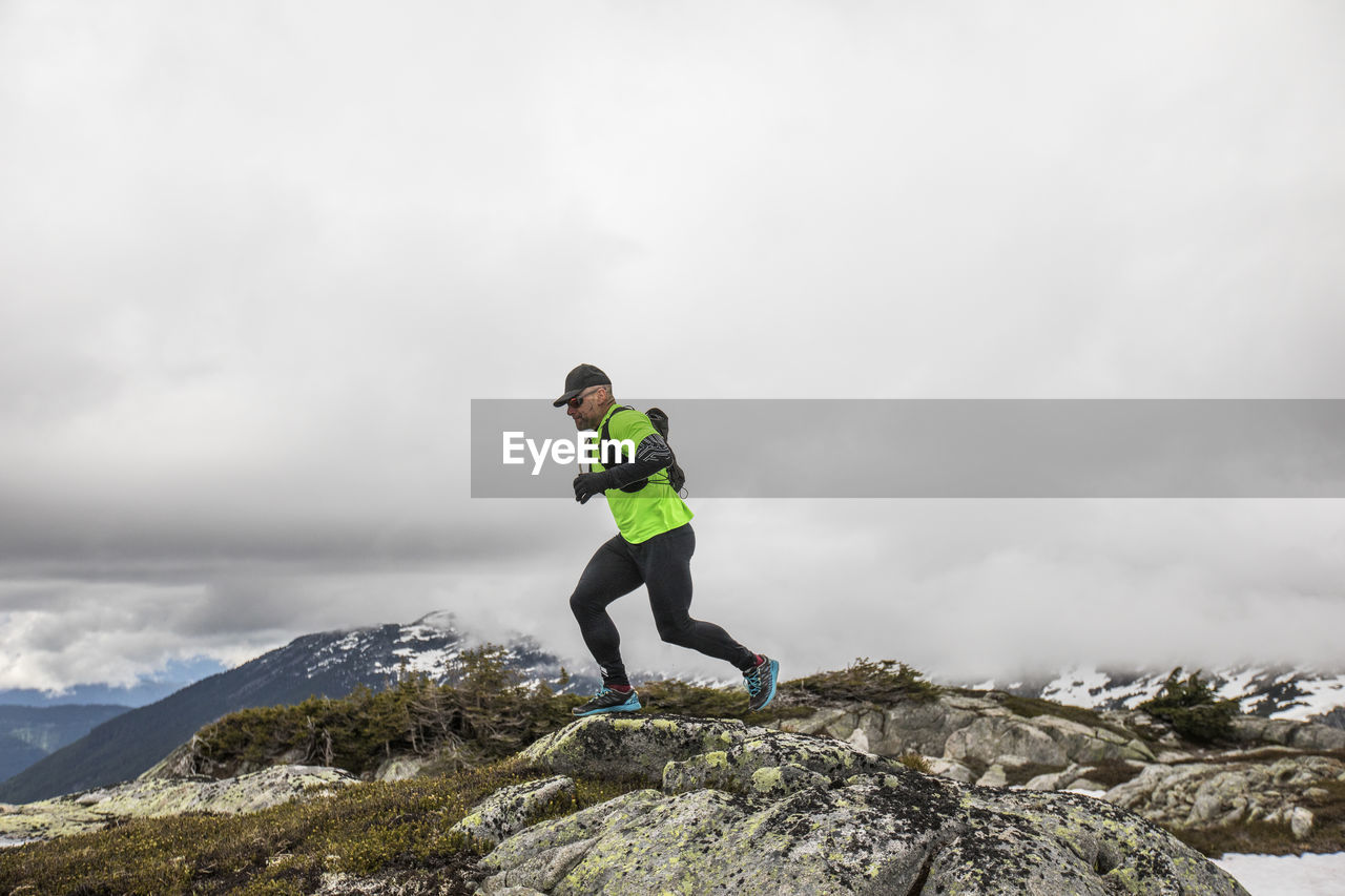 Side view of fit active man trail running on mountain ridge.