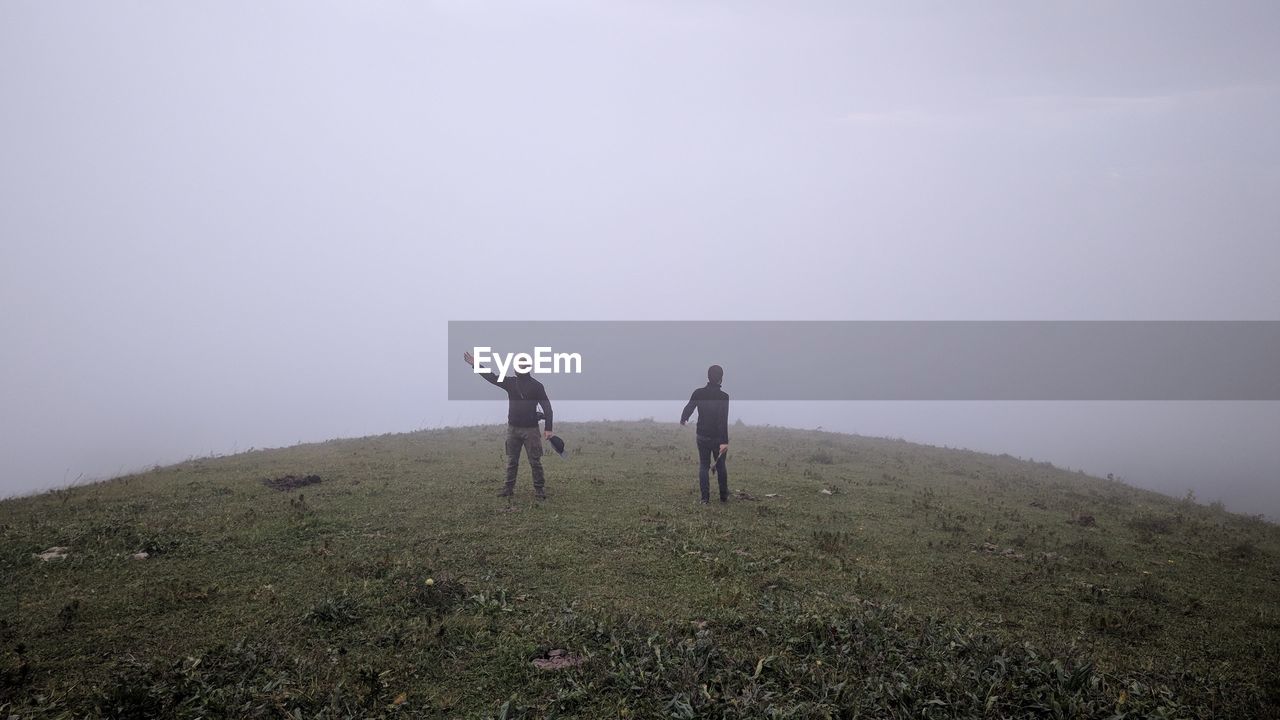 REAR VIEW OF MEN WALKING ON LANDSCAPE AGAINST SKY DURING FOGGY WEATHER
