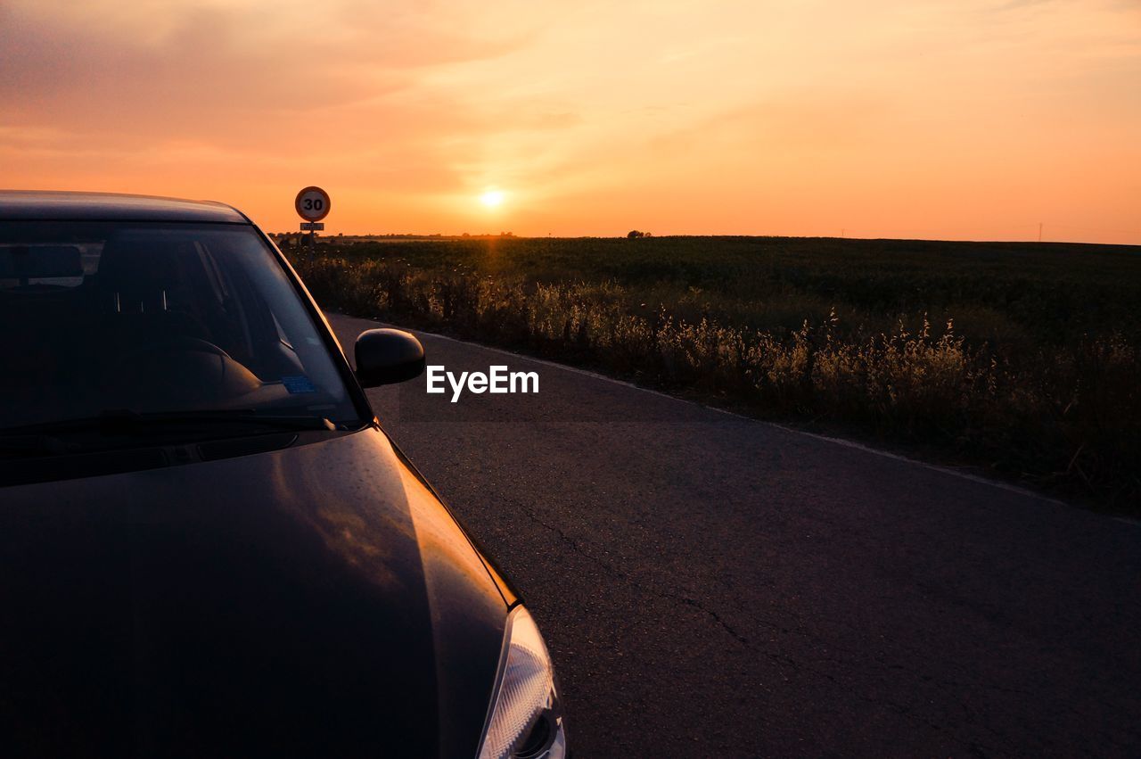 Cropped image of car on road by field against sky during sunrise