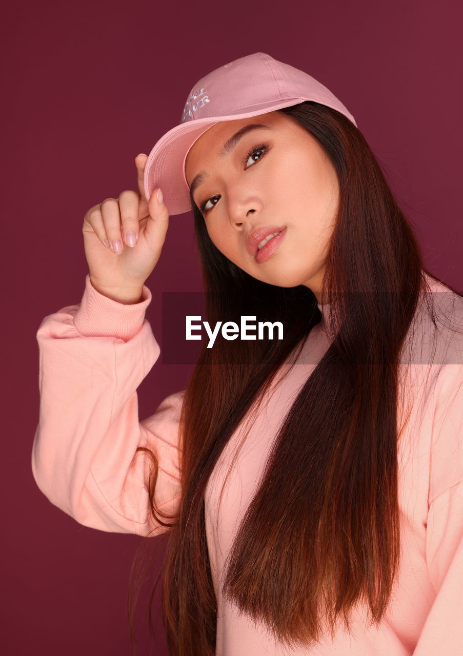 Portrait of serious young asian woman in the studio wearing pink clothes over garnet background